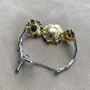 Detailweergave van een zilveren gedraaide armband met drie gouden madeliefjes op een grijze stof.
