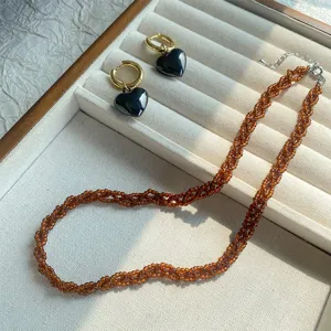 Detailaufnahme: Perlenhalskette in Milchtee-Farbe und goldene Creolen mit schwarzen Herzen