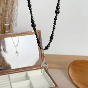 Detail view of a creative silver-toned fork pendant on a stylish black beaded necklace chain