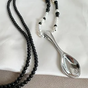 Detailed view of a creative silver spoon pendant on a black and white beaded necklace chain.