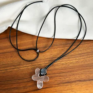 Close-up detail of clear acrylic flower pendant on a long black cord sweater necklace.