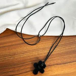 Detail of a minimalist black hollow flower pendant on a long black cord necklace.