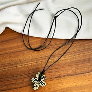 Close-up detail of a minimalist spotted flower pendant necklace with adjustable black cord