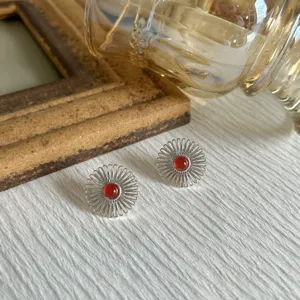 Dettaglio di orecchini a fiore in argento con agata rossa su trama bianca.