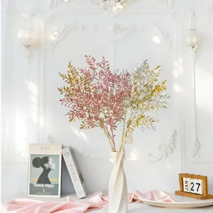 Glittering three-forked artificial bamboo leaf sprigs in a white vase for home decor.