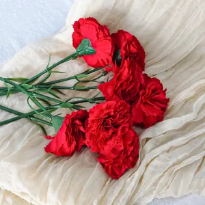 Primer plano de claveles rojos artificiales sobre una tela beige texturizada decorativa