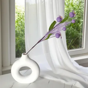 Branche de pavot mauve artificielle dans un vase rond en céramique blanche moderne.