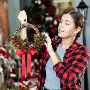 Handmade Christmas wreath with vibrant red berries, pinecones, and a red bow decoration.
