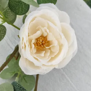 Close-up of white artificial camellia flower with realistic green eucalyptus leaves