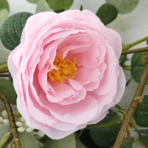Detailed macro view of a realistic pink silk camellia flower head with lush green leaves