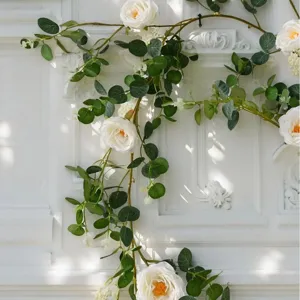 Detail view of elegant artificial white rose and eucalyptus leaf vine on white wall