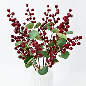 Artificial red berry branches with green leaves in a white ceramic vase decoration