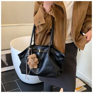 Dettaglio di grande borsa tote vintage nera con ciondolo a orso, tenuta da persona