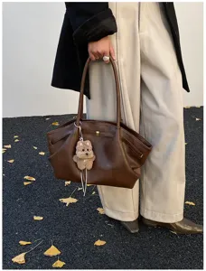 Grande borsa tote marrone stile vintage tenuta da una modella con foglie autunnali cadute