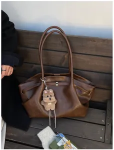 Dettaglio della borsa tote in pelle marrone vintage con portachiavi a orsetto.
