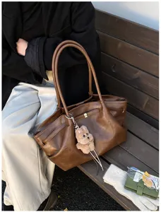 Dettaglio di una borsa tote vintage marrone con ciondolo a orsetto su una panca.