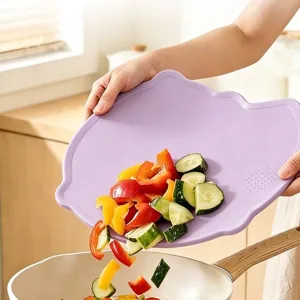 Durable and flexible purple TPU cutting board being used to pour vegetables into a pan