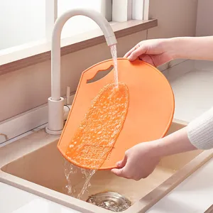 Premium D-shaped orange TPU cutting board being rinsed under kitchen faucet water