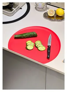 Close-up of a red D-shaped TPU cutting board with cucumber slices in a kitchen