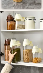 Hand grabbing a large airtight plastic container for grains in a kitchen cabinet.