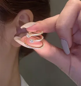 Detail view of a sparkling triple-layer gold-tone zircon ear cuff held against a human ear.