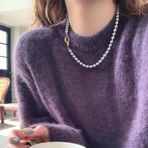 Detailweergave van een elegante grijze parelketting met gouden sluiting op paarse trui