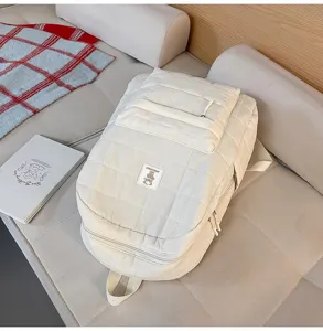 Esthetische crème gewatteerde rugzak op een minimalistische bank met lifestyle rekwisieten