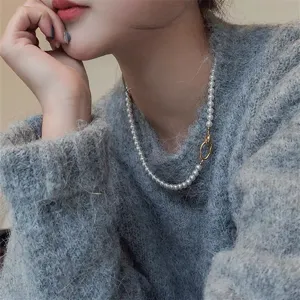 Elegante witte ronde parelketting met gouden ovale sluiting op een grijze pluizige trui