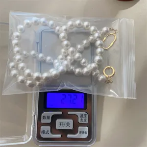 Detailopname van een ronde witte parelketting met een gewicht van 27,21 g op de schaal