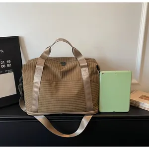 Large brown checkered travel duffel bag displayed with a tablet for size comparison.