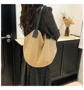 Detailopname van de beige gewoven schoudertas gedragen door een model binnenshuis.