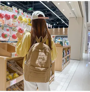 Achteraanzicht van een vrouw met een kaki gewatteerde rugzak met ruitpatroon in een winkel