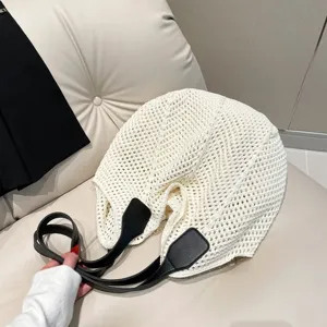 Detail van witte gehaakte tote tas met zwarte leren banden op zachte achtergrond.