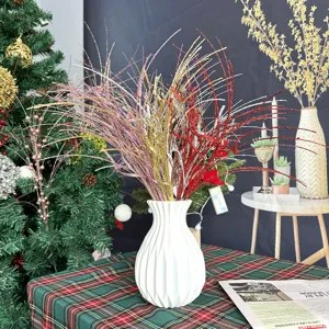 Détail de branches pailletées festives dans un vase blanc pour décorer le sapin de Noël