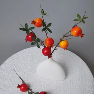 Primo piano di un ramo di melograno artificiale in vaso bianco per decorazione casa.