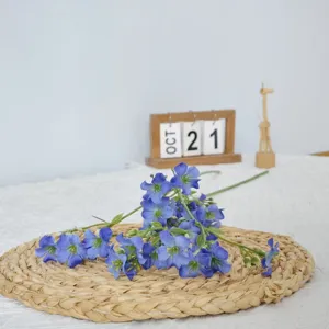 Primer plano detallado de flores artificiales de seda azul dispuestas en estera tejida.