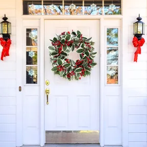 Holly leaf and red berry Christmas wreath hanging on a white front door background