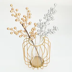 Close-up detail of artificial gold and silver berry branches inside a modern gold wire vase.