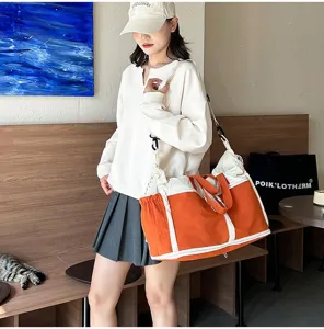 Detail view of the large orange travel bag being carried by a model in a cozy cafe.