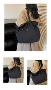Back view of a large black waterproof shoulder bag worn by a model in a beige coat
