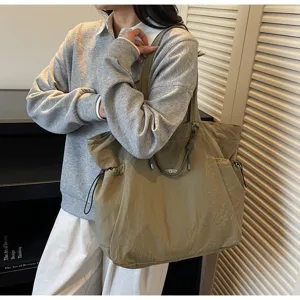 Large olive nylon tote bag with drawstring detail worn by a model in a casual indoor setting