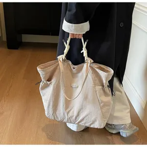 Detailed view of a large beige travel tote bag carried by a model in a casual setting.