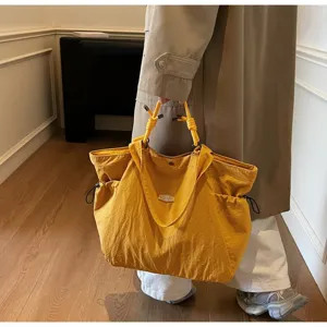 Large capacity yellow waterproof travel tote bag carried by a model in a trench coat.