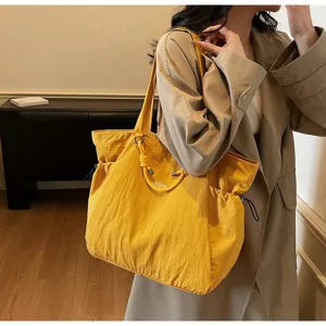 Yellow waterproof large capacity travel tote bag worn by a model in a trench coat