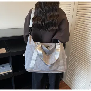 Back view of a grey striped large capacity travel bag worn over the shoulder by a model