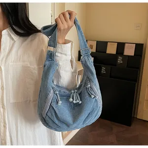 Close-up detail of large denim dumpling bag with zippers and tassels carried by a model