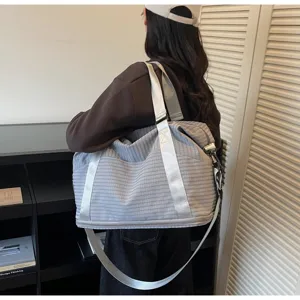 Gray plaid travel bag worn over the shoulder by a model in a stylish modern indoor setting.