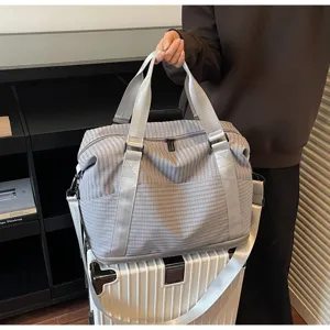 Lifestyle detail of a large capacity checkered travel bag resting on a white suitcase