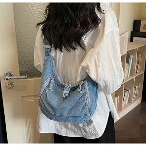 Blue denim crescent crossbody bag shown from behind on a model in a casual setting