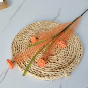 Vue détaillée de branches de roseaux artificiels avec fleurs orange sur un tapis en paille tressée.